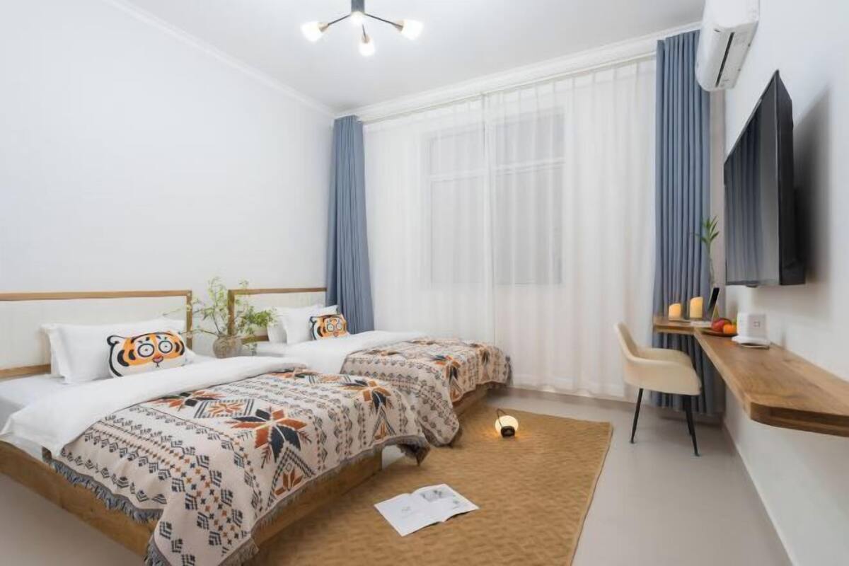 Une chambre d’hôtel avec deux lits, un bureau, une chaise, une télévision et une fenêtre avec des rideaux.
