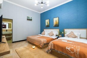 A hotel room with two beds, a television, a desk, and artwork on the walls.