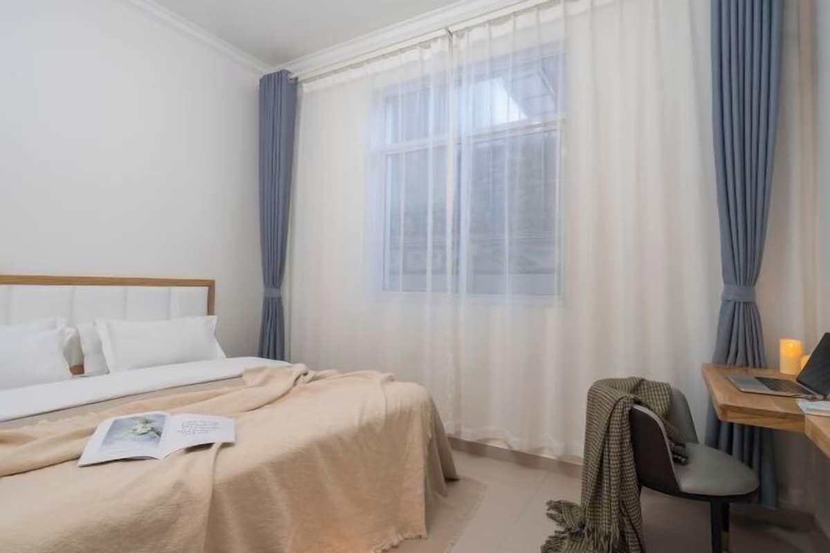 A hotel room with a bed, a desk with a laptop, and a window with curtains.