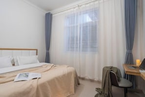 A hotel room with a bed, a desk with a laptop, and a window with curtains.