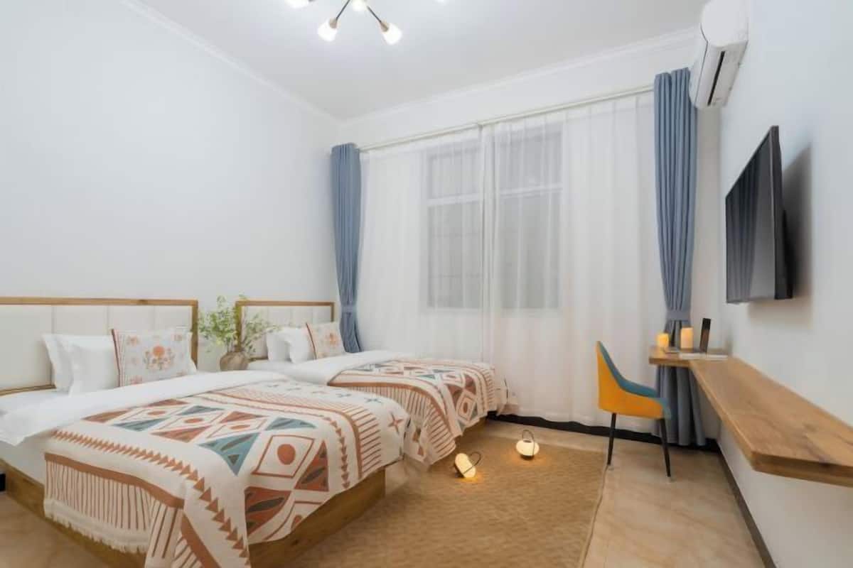 Une chambre avec deux lits, un bureau, une chaise, une télévision et une fenêtre avec des rideaux.