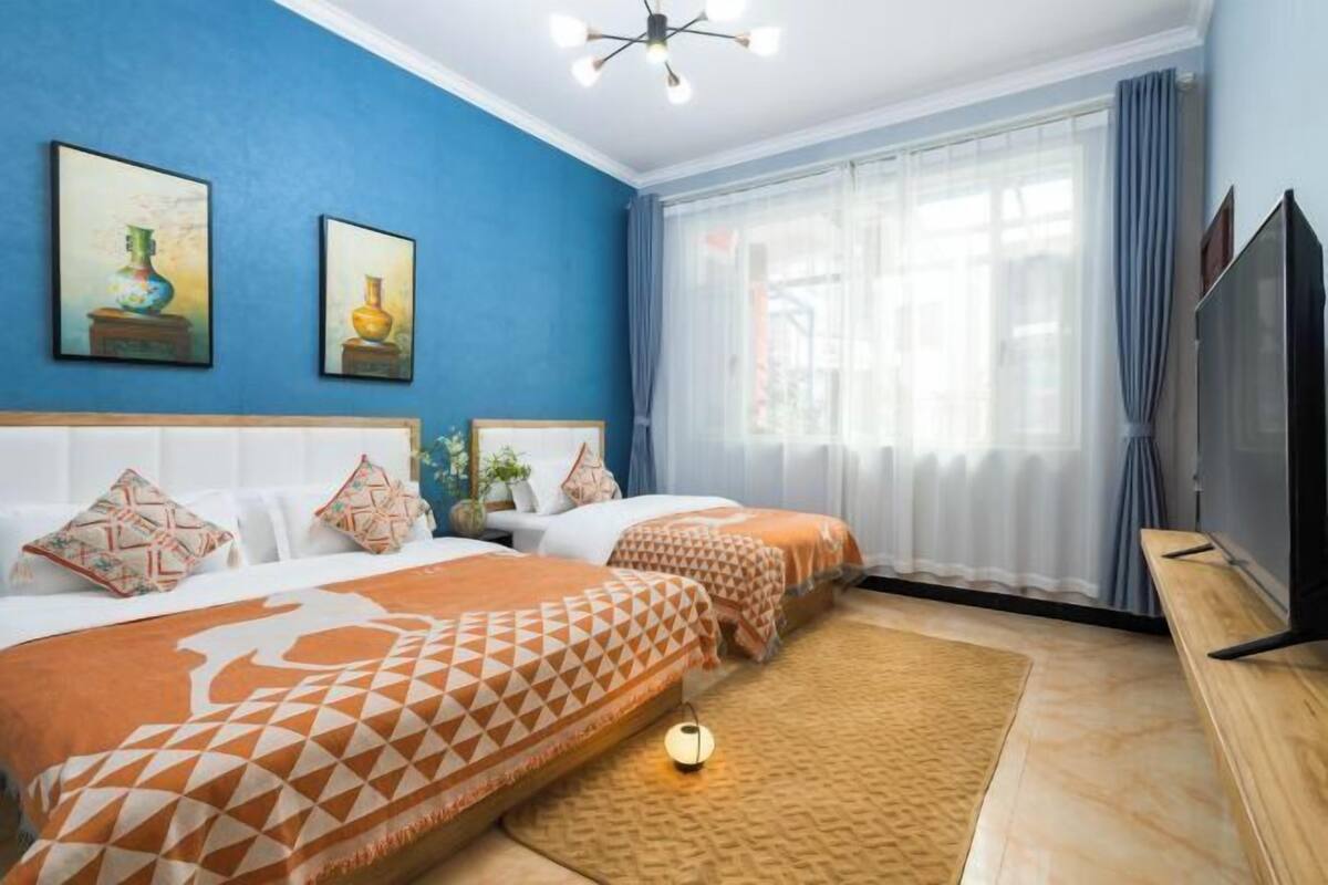Une chambre d’hôtel avec deux lits, une télévision, une grande fenêtre avec des rideaux et des œuvres d’art accrochées au mur.