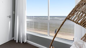 Una habitación con un ventanal grande que da a la playa, una silla de mimbre y una puerta con manija.