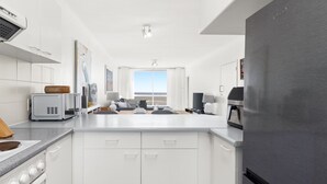 Una cocina moderna con armarios blancos, un refrigerador de acero inoxidable y vistas al exterior.
