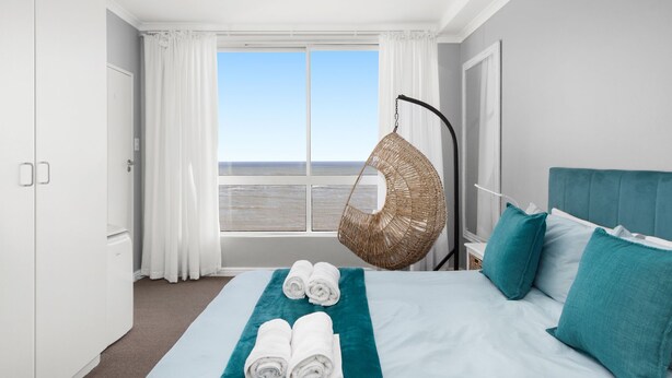 Una habitación de hotel con cama, una silla colgante y vista al mar.