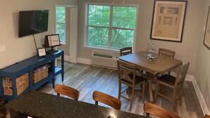 A dining area with a wooden table and chairs, a ceiling fan, and a large window with a view of trees. - Deluxe 2700 sqft 3 bed 4 bath Villa in Boone, NC (Boone)