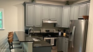 A modern kitchen with grey cabinets, stainless steel appliances, and a wooden bar stool. - Deluxe 2700 sqft 3 bed 4 bath Villa in Boone, NC (Boone)