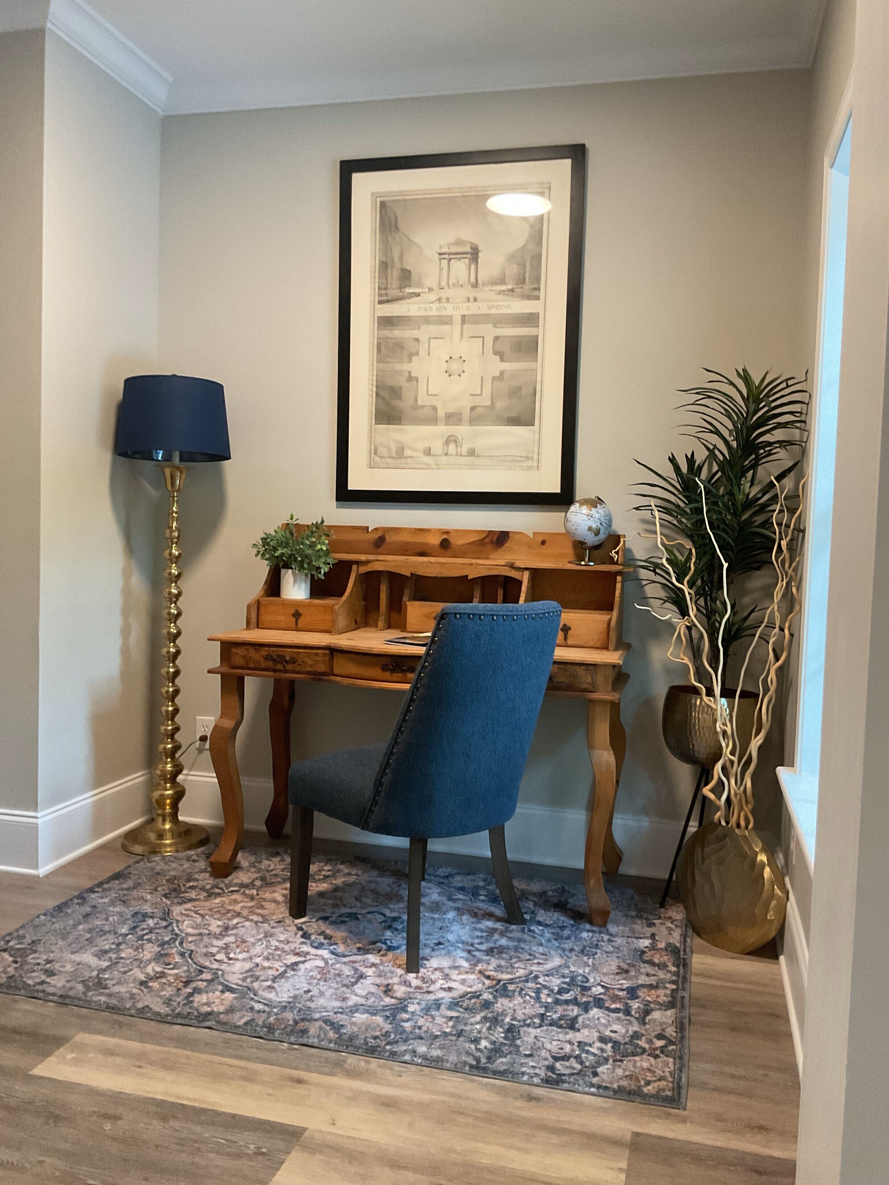 A study area with a desk, chair, lamp, framed artwork, and potted plants.