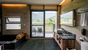 A modern bathroom with a bathtub, a sink, a mirror, and a view of mountains through a sliding door. - The Silence Manor (Hualien)