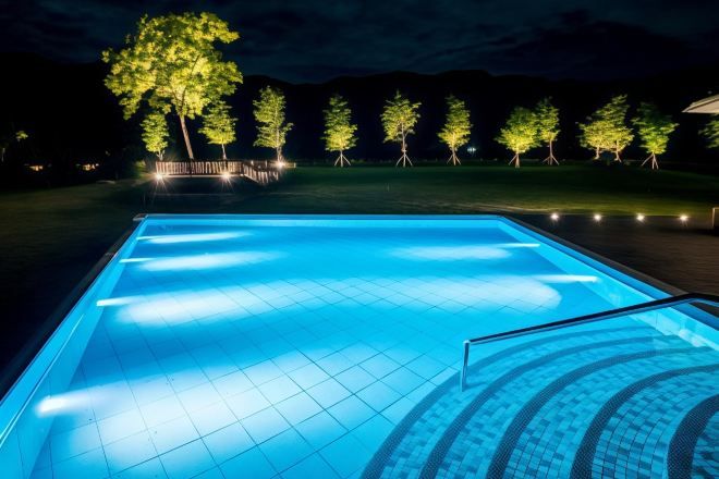 A swimming pool at night with illuminated tiles and trees in the background.