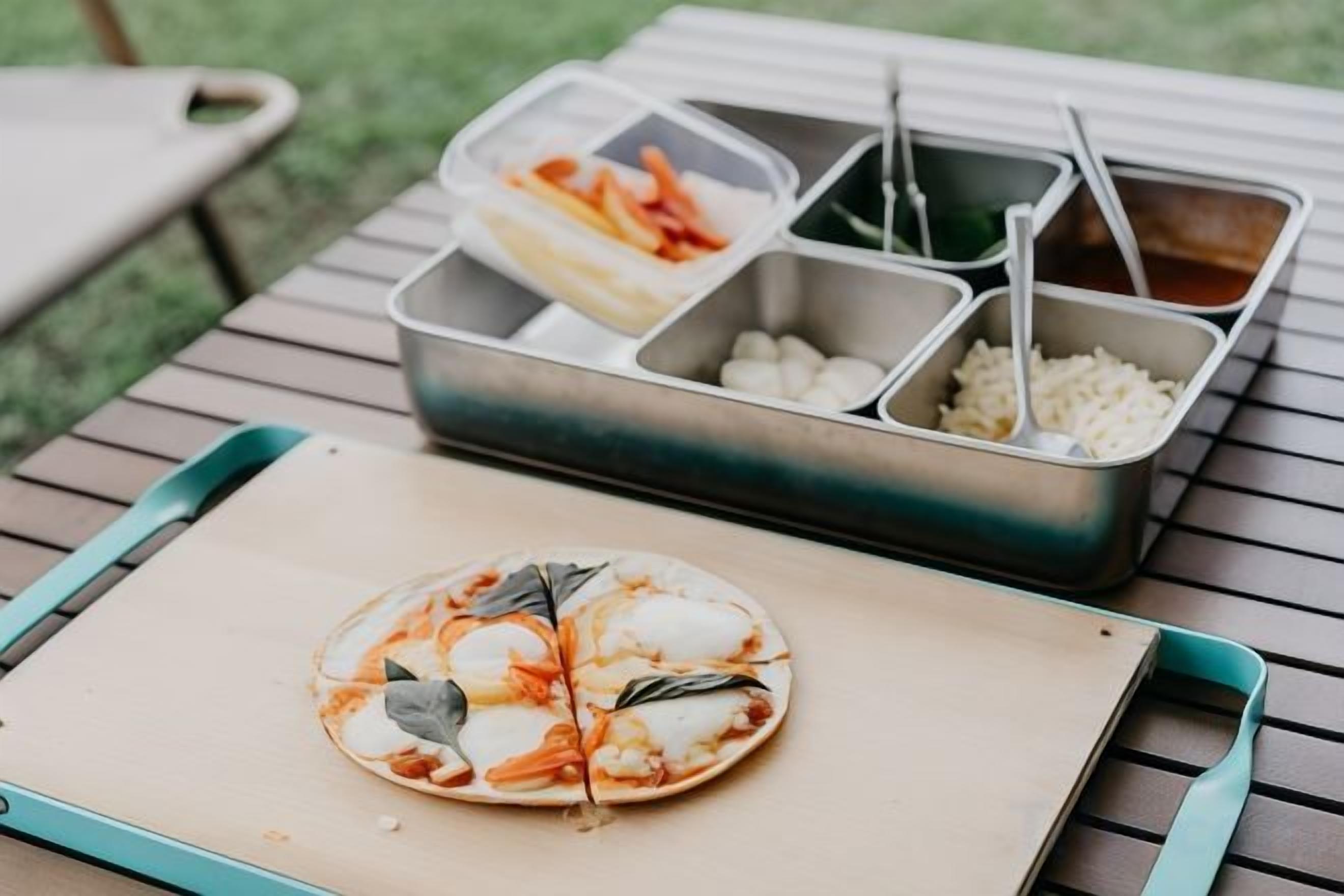 A meal setup with a pizza on a tray, a salad container, and a rice container on a table.