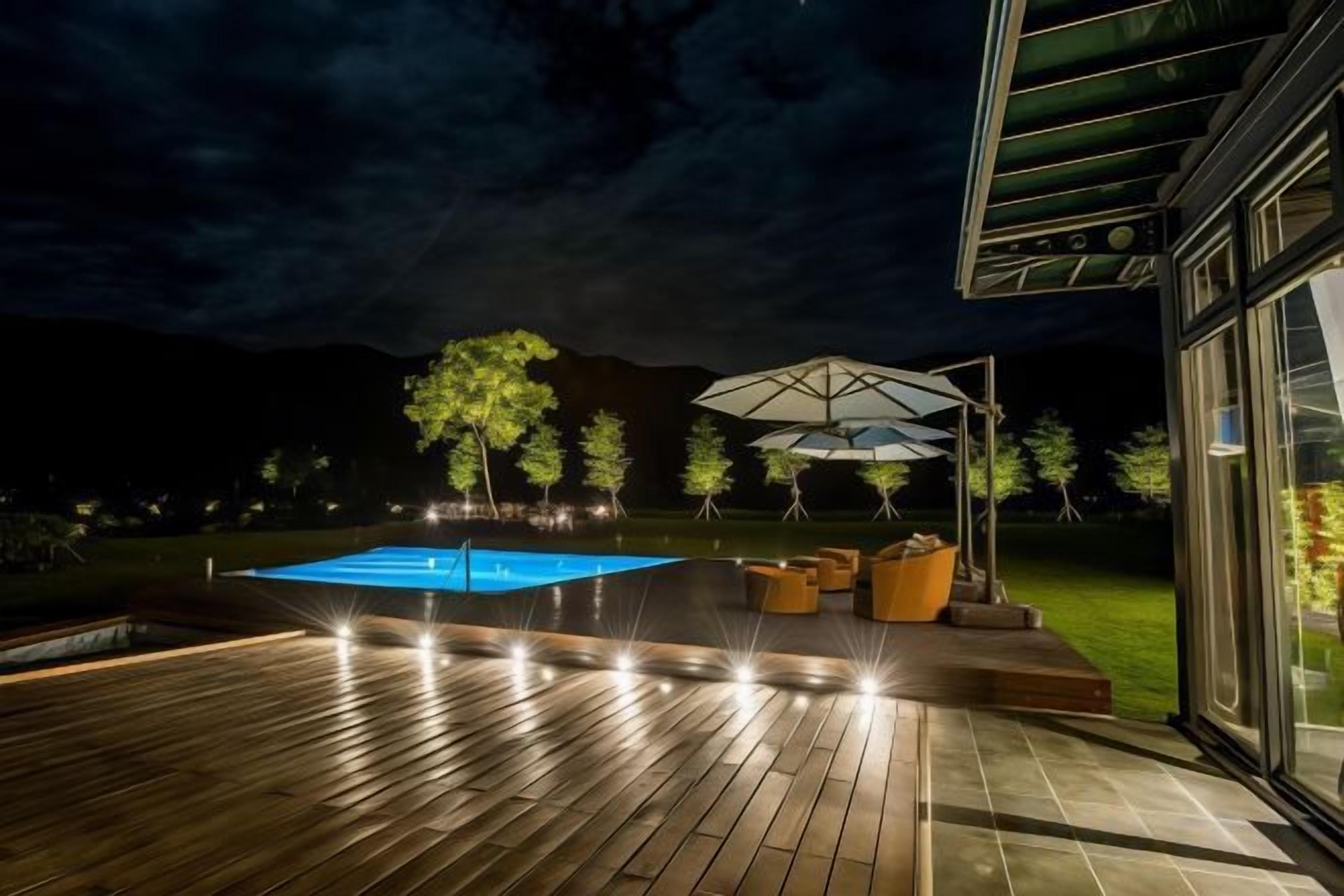 A wooden deck with a swimming pool, outdoor furniture, and a glass building.