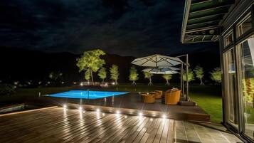 A wooden deck with a swimming pool, outdoor furniture, and a glass building.