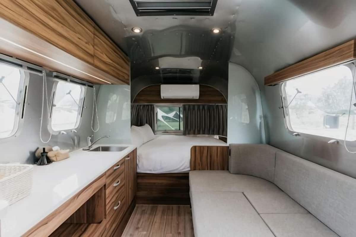 A compact RV interior with a kitchenette, a bed, and a seating area.