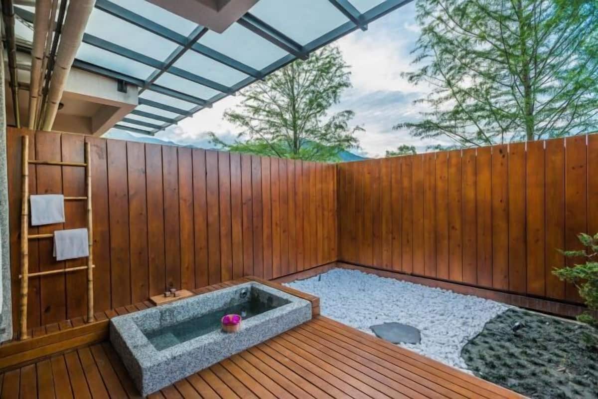 A wooden deck with a hot tub, a small seating area, and a glass ceiling.