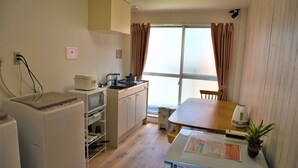 Une cuisine compacte équipée d’un four à micro-ondes, d’une cuisinière et d’un évier, une table à manger avec des chaises, et une grande fenêtre avec des rideaux.