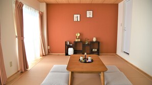 Une pièce avec un sol recouvert de tatamis, une table en bois, des coussins, une petite étagère avec des objets décoratifs et une porte coulissante.
