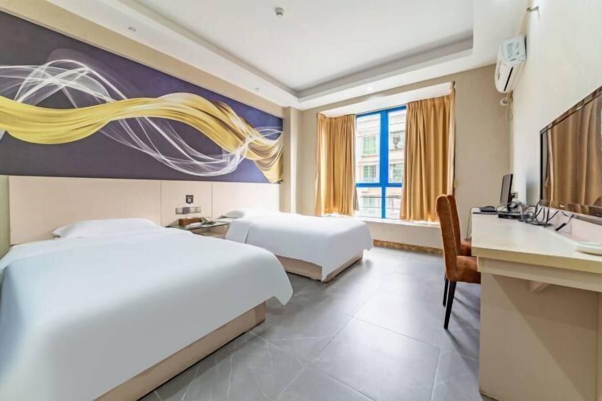 A hotel room with two beds, a desk, and a window with curtains.