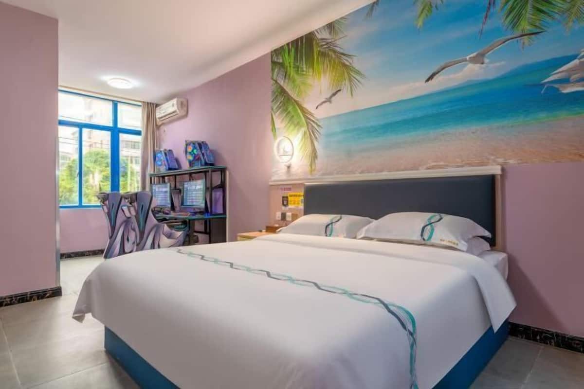 A bedroom with a bed, a desk with a computer, and a wall mural of a beach scene.