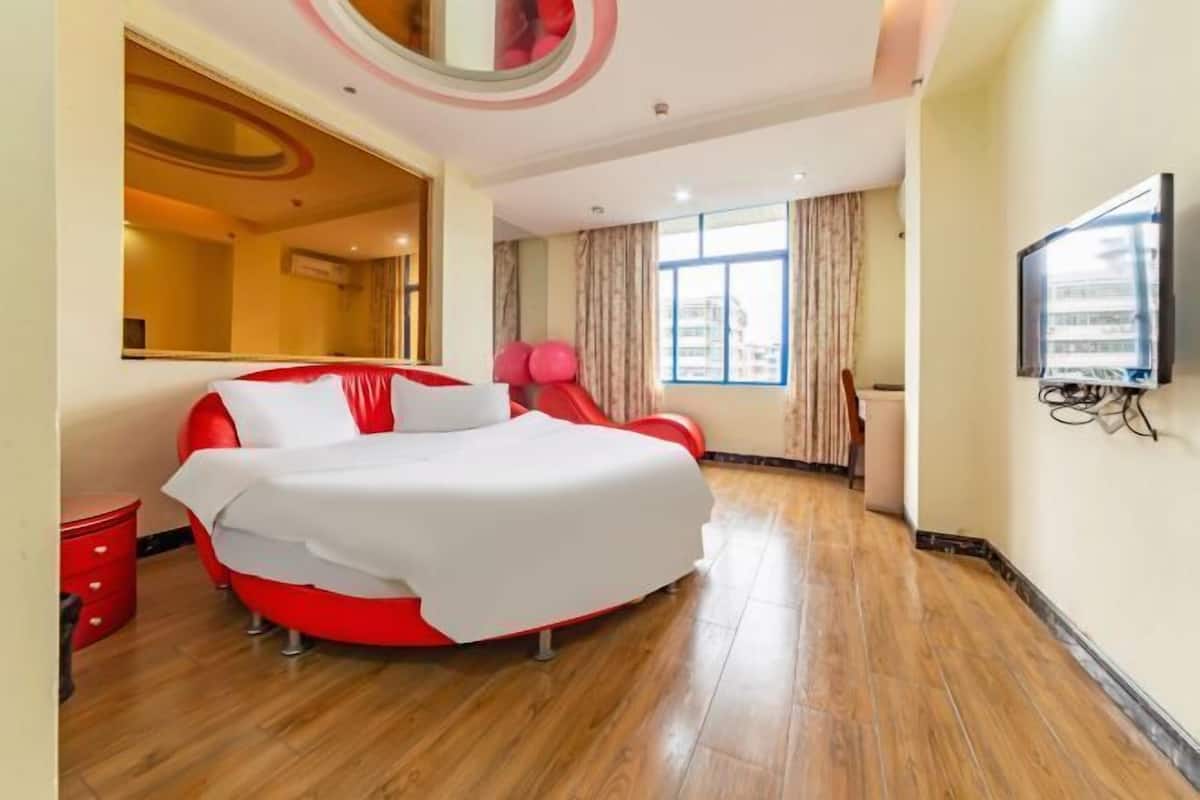 A hotel room with a large bed, a television, a window with curtains, and a red chair.