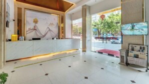 A hotel reception area with a marble counter, a large abstract painting, a television screen, and a glass door leading outside. - Xingqiba Business Hotel Maoming (Maoming)