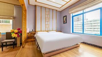 Una habitación de hotel con una cama grande, un escritorio, una silla, un ventanal con vistas a la ciudad y suelo de madera.