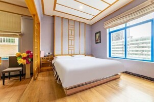 Una habitación de hotel con una cama grande, un escritorio, una silla, un ventanal con vistas a la ciudad y suelo de madera.