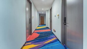 A hotel hallway with a colorful carpet, doors on both sides, and a wooden door at the end. - Xingqiba Business Hotel Maoming (Maoming)