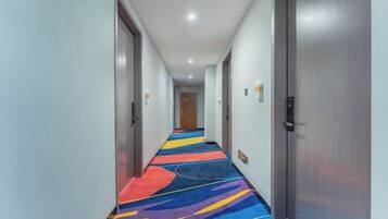 A hotel corridor with a colorful carpet, doors on both sides, and a light-colored ceiling.