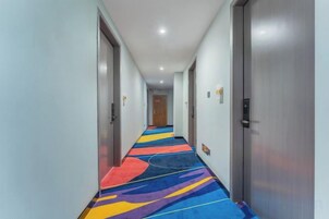 A hotel corridor with a colorful carpet, doors on both sides, and a light-colored ceiling.