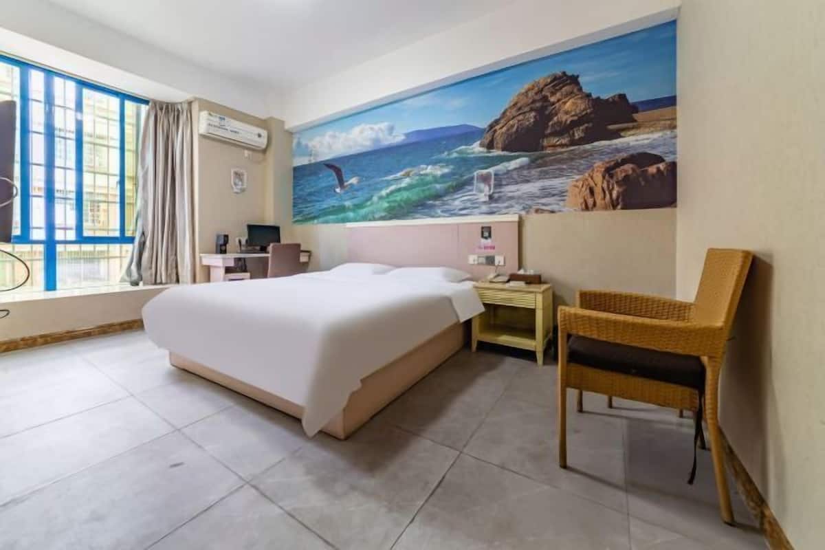 A hotel room with a bed, a desk, a chair, and a large painting of a beach scene.