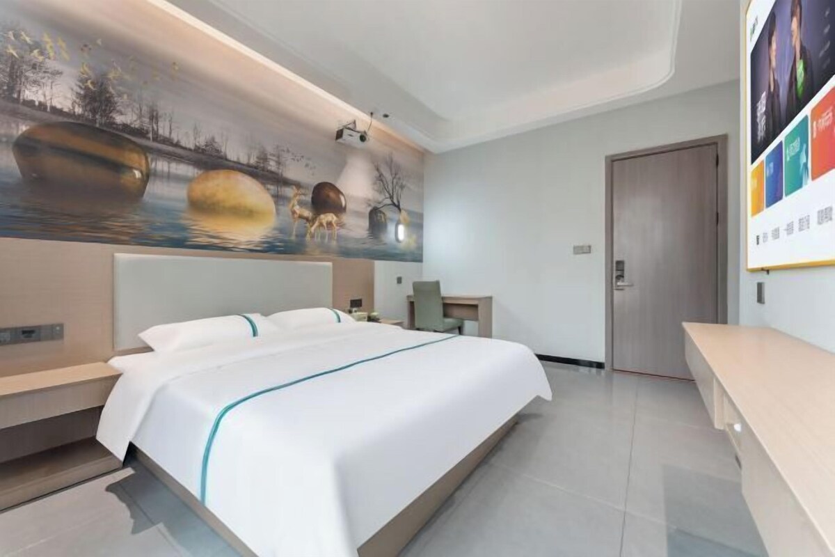 A modern hotel room with a large bed, a desk, and a mural on the wall.