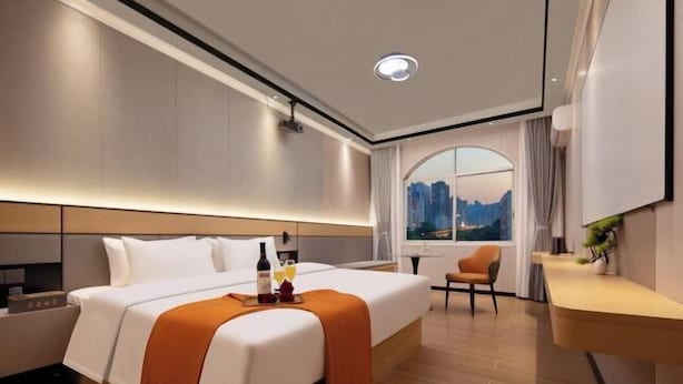 A modern hotel room with a large bed, a bedside table, a small desk, and a window with a city view. - Xingqiba Business Hotel Maoming (Maoming)