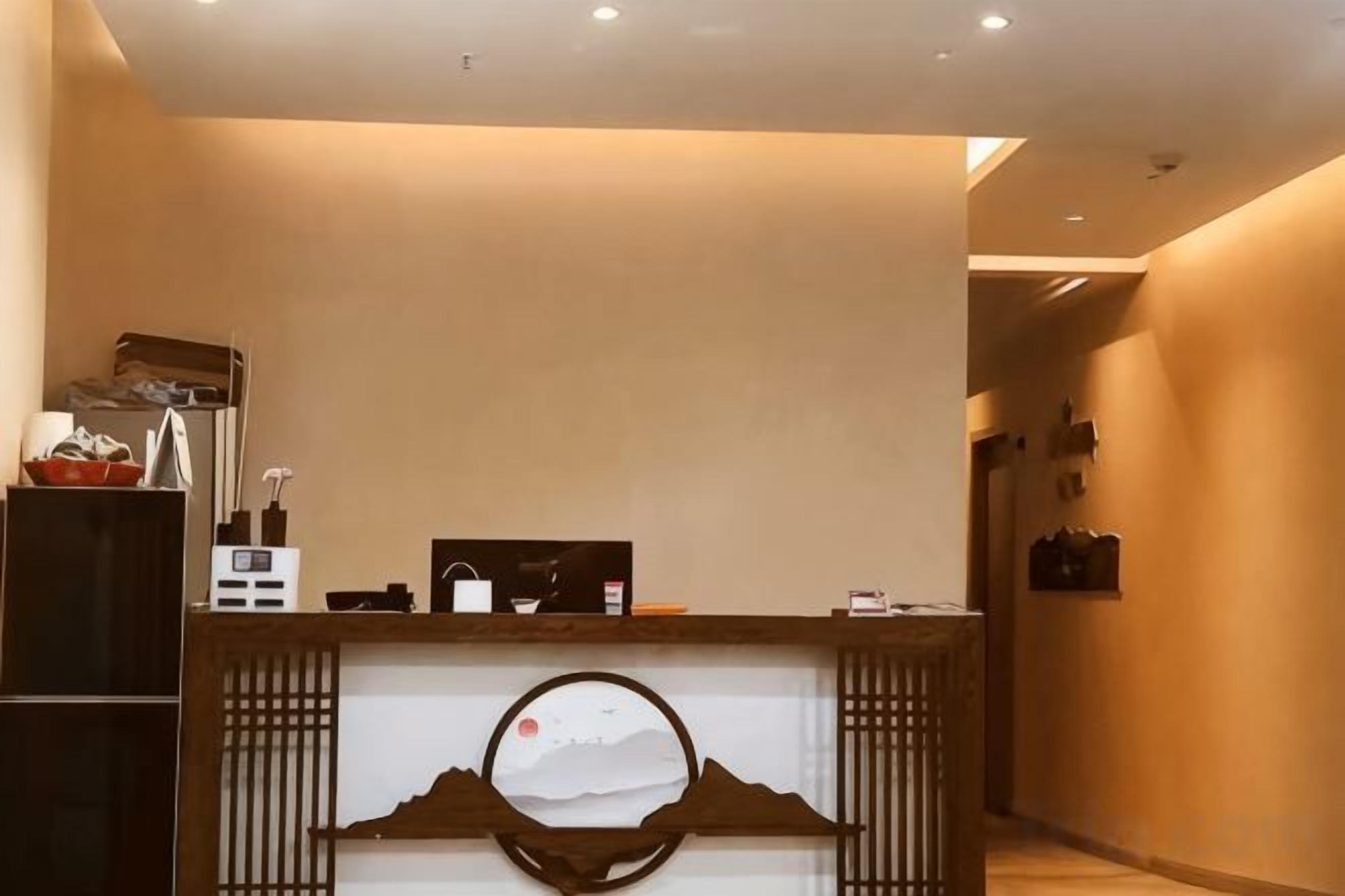 A reception desk with a wooden counter, a white wall with a circular decoration, and a hallway leading to another room.