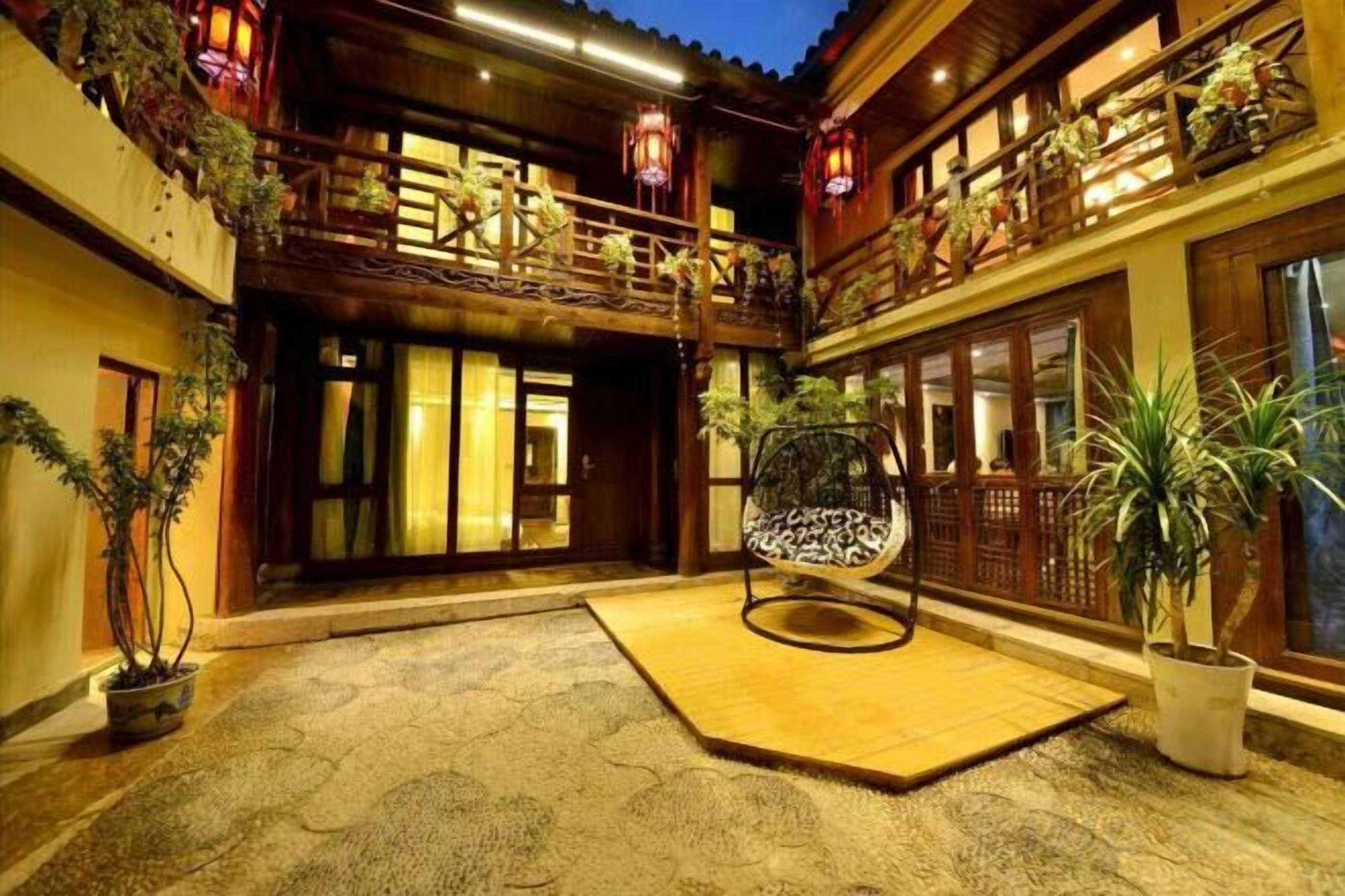 A traditional courtyard with a wooden balcony, potted plants, and a hanging chair.