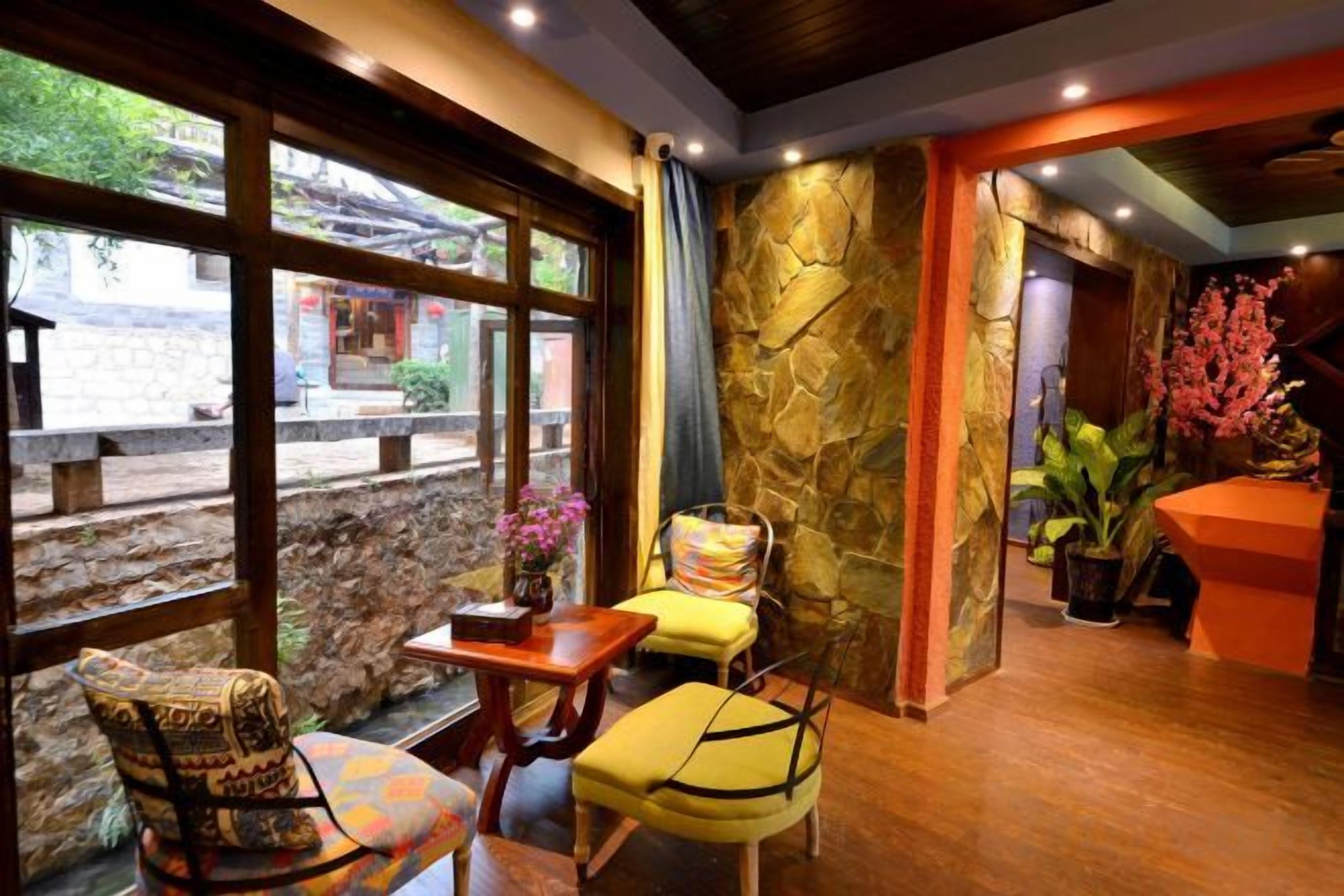 A room with a stone wall, a wooden floor, a table with chairs, and a view of the outside.