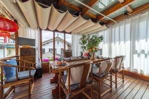 A wooden deck with a dining table and chairs, a potted plant, and a view of buildings through large windows. - Qiyu Yijingwan Inn (Lijiang)