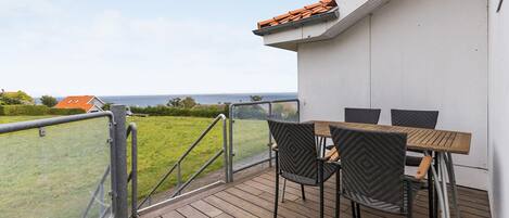 A deck with a table and chairs, overlooking a grassy area and a body of water.