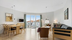 A modern living room with a dining area, a sofa, and a TV. - Gudhjem Søpark Lejl. 18 (Gudhjem)