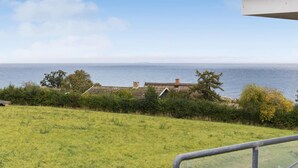 A coastal view with a grassy field, a building with a sloped roof, and the sea in the background. - Gudhjem Søpark Lejl. 18 (Gudhjem)