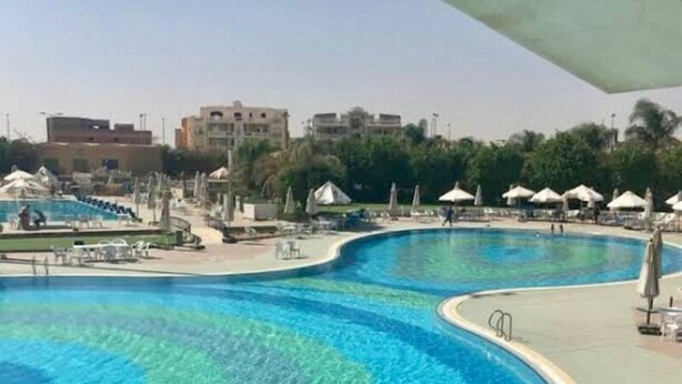 A large, curved swimming pool with clear blue water, surrounded by lounge chairs and umbrellas. - Madinaty (New Cairo)