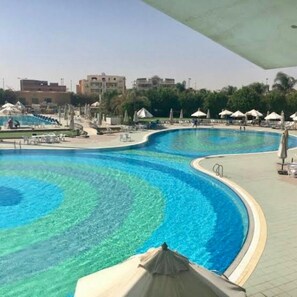 A large, curved swimming pool with clear blue water, surrounded by lounge chairs and umbrellas.