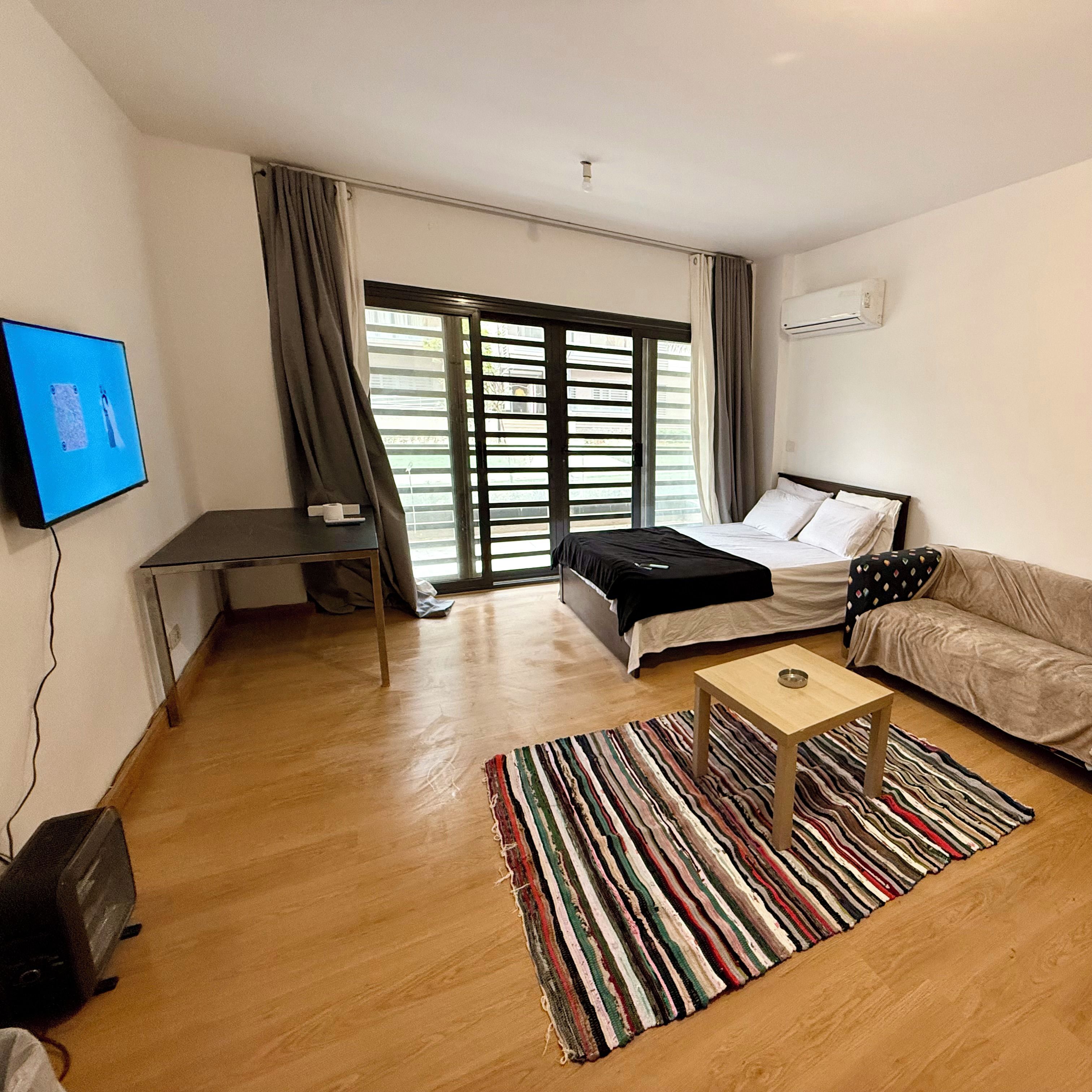 Una sala de estar moderna con cama, sofá, televisor y ventana con cortinas.