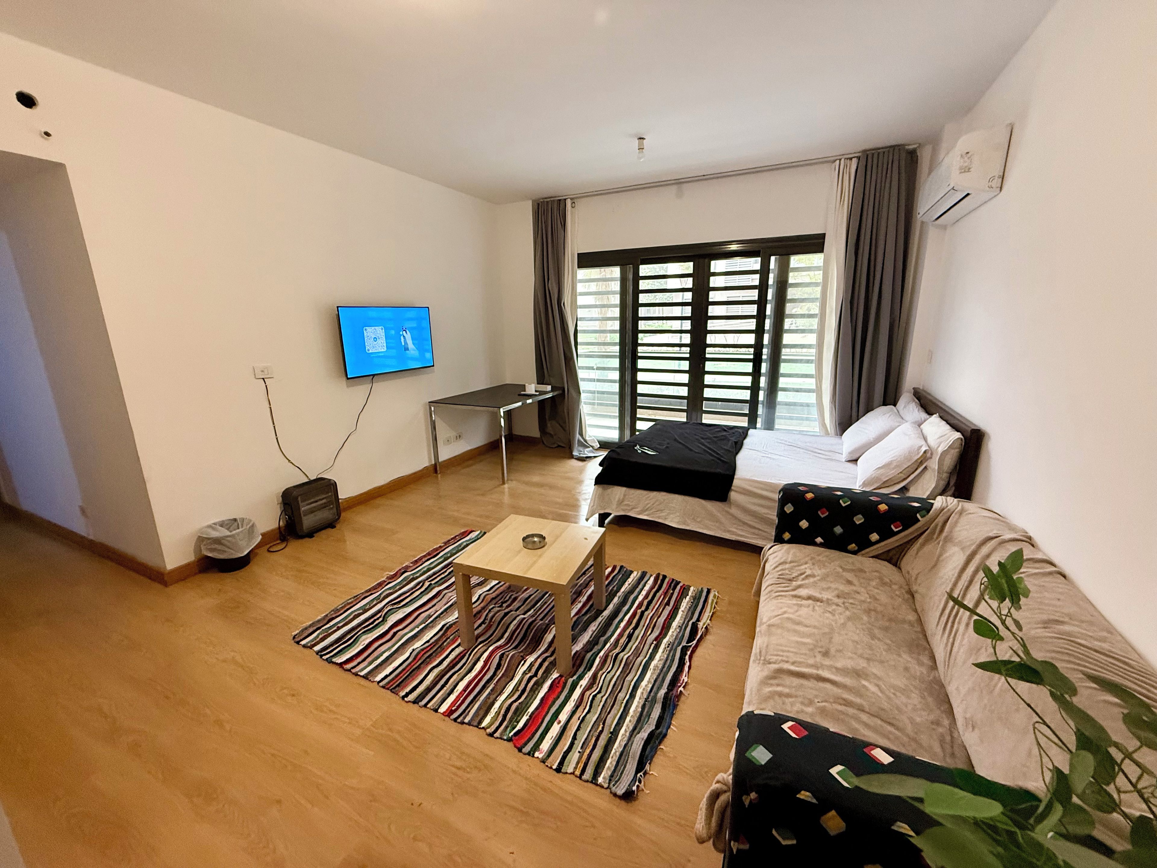 Habitación de hotel moderna con cama, sofá, televisor, escritorio y ventana con cortinas.