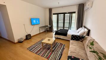 Habitación de hotel moderna con cama, sofá, televisor, escritorio y ventana con cortinas.