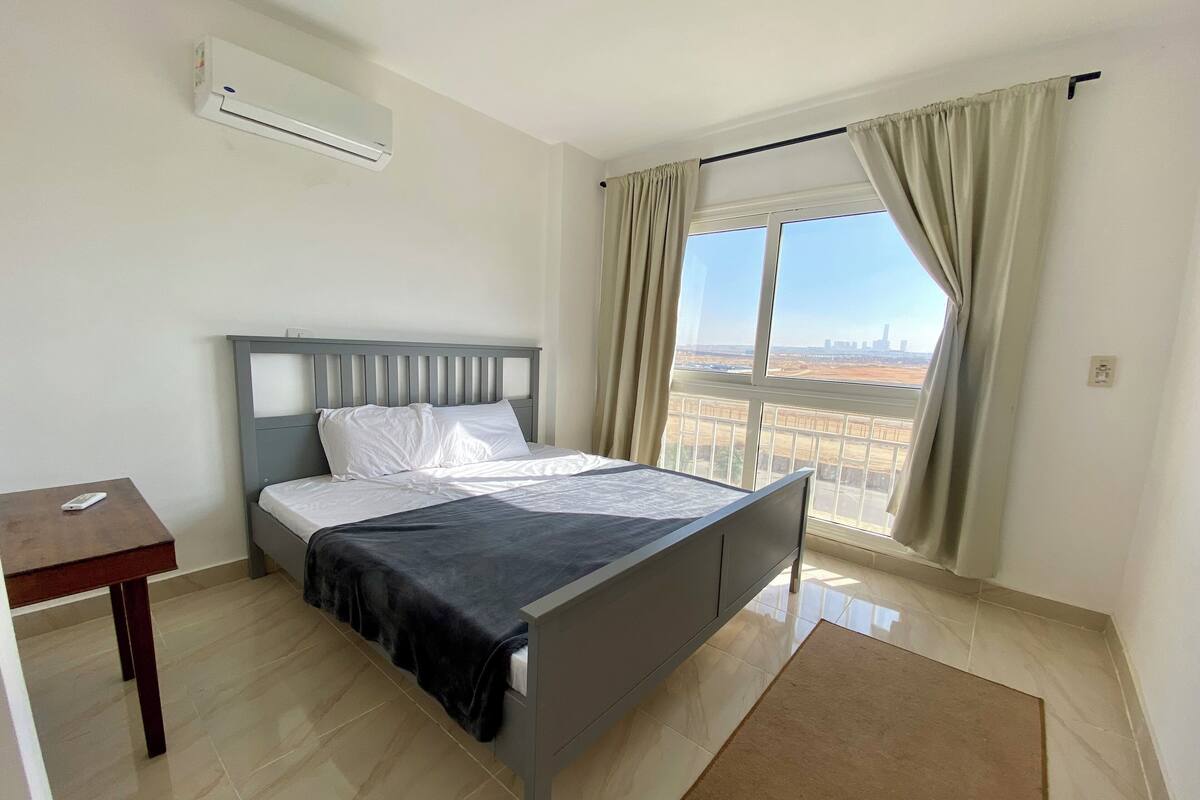 Une chambre à coucher avec un lit, un bureau, un climatiseur et une fenêtre avec des rideaux.