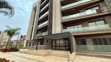 A modern multi-story building with balconies, a covered entrance, and a landscaped area with plants.