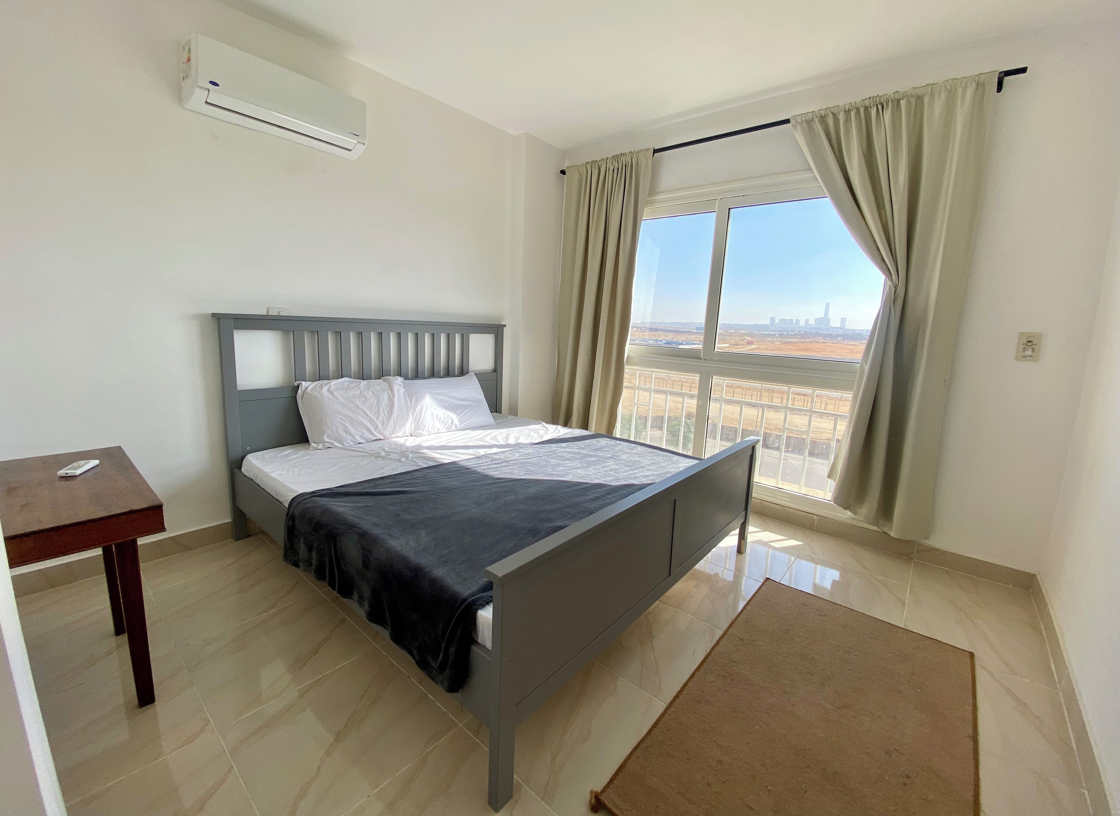 A bedroom with a bed, a desk, an air conditioner, and a window with curtains.