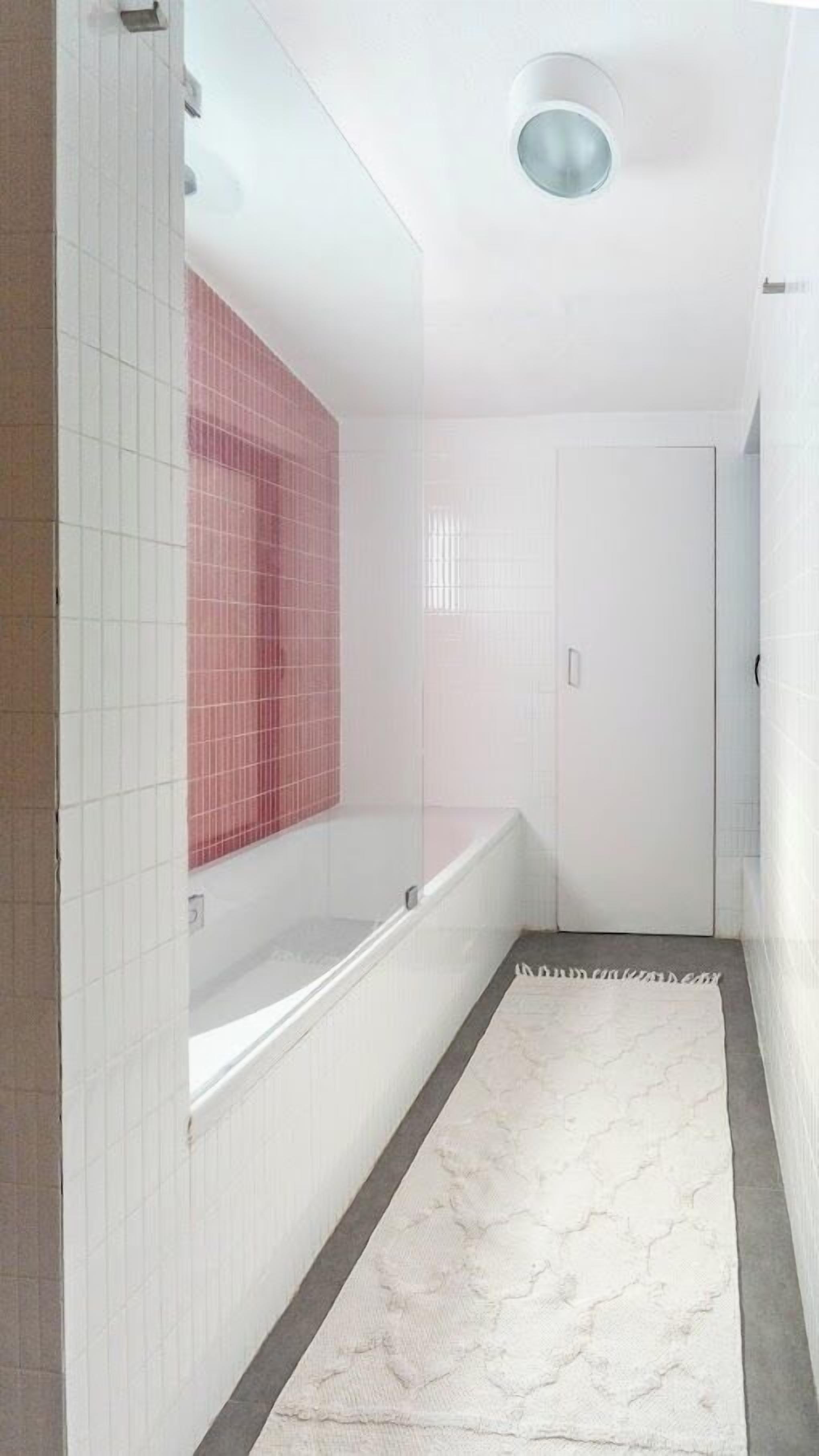 Une salle de bain moderne avec une baignoire blanche, un espace de douche carrelé en rose et un tapis à motifs de marbre.