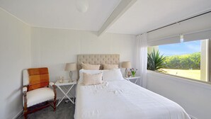 A bedroom with a large bed, a chair, two bedside tables, and a window with a view of greenery. - Breathtaking views over Bridgewater Bay (Cape Bridgewater)